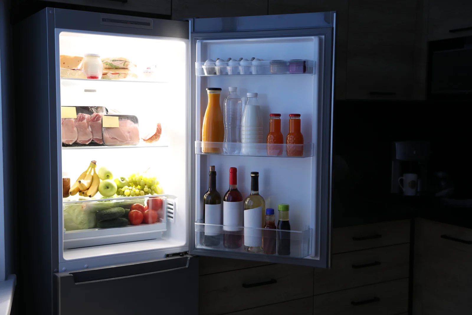 Fridge-freezer standing open in a dark kitchen, fully stocked and cooling properly
